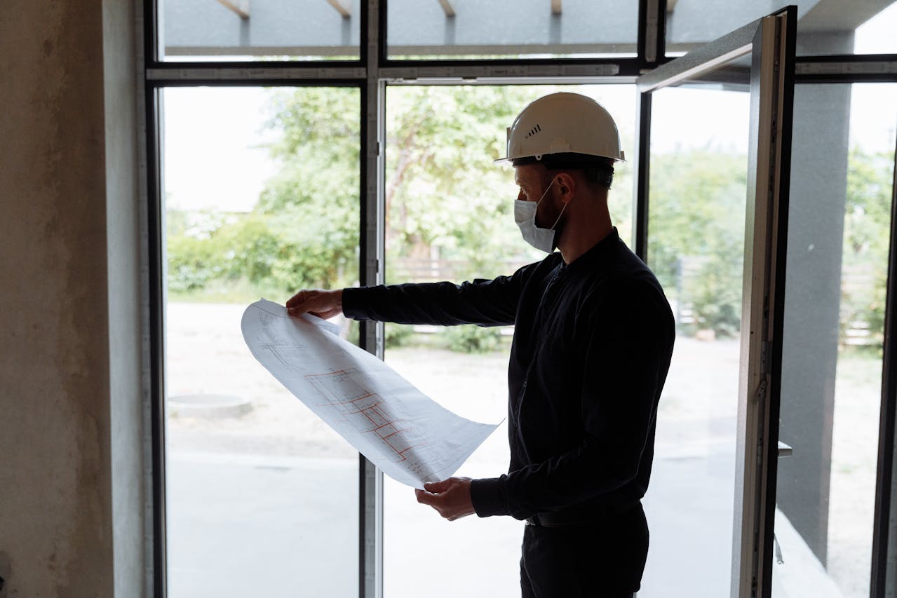 professional looking at building plans wearing a hardhat and mask